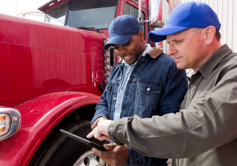 A fleet manager and a driver looking at a tablet in front of a truck.